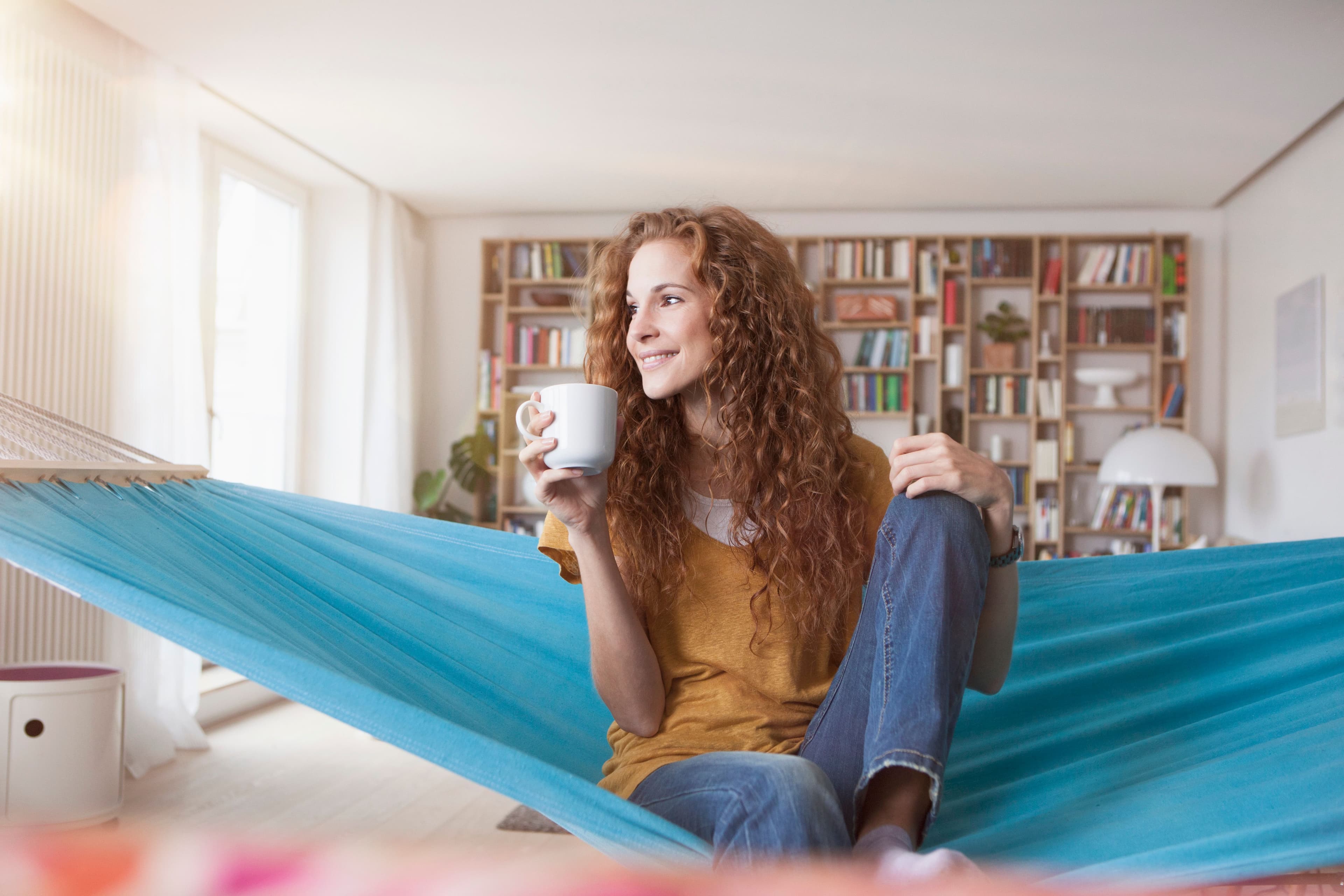 a woman is sitting in a hammock holding a cup of coffee .