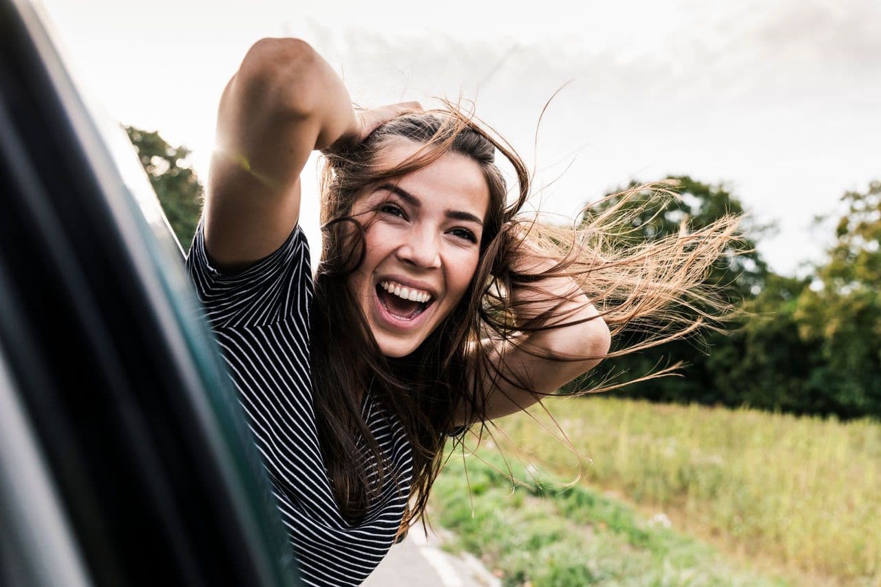 a woman is sticking her head out of a car window and smiling .