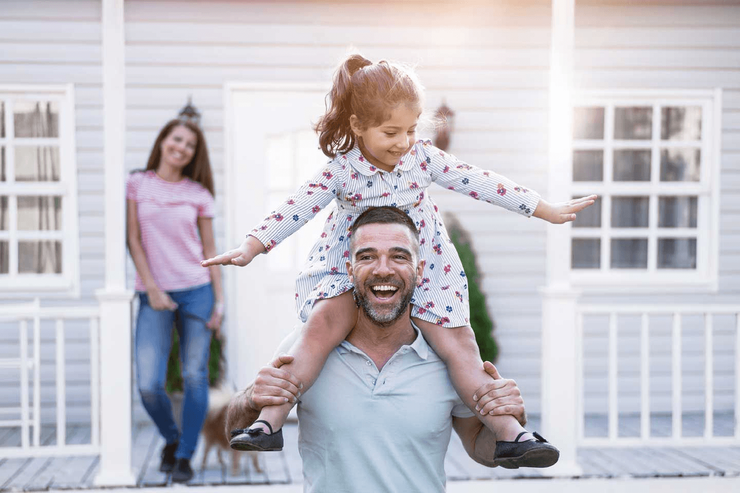 a man is carrying a little girl on his shoulders in front of a house