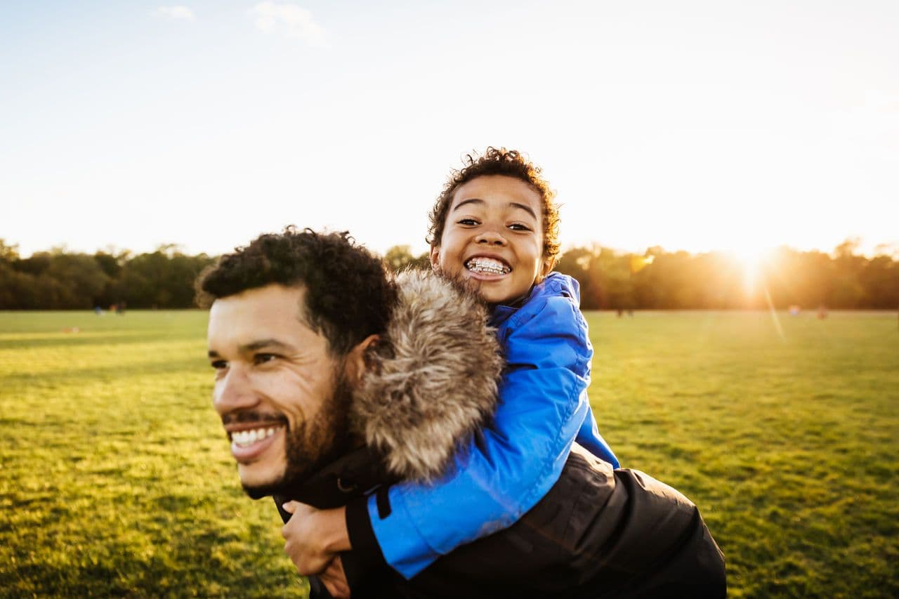a man is carrying a little boy on his back in a park .