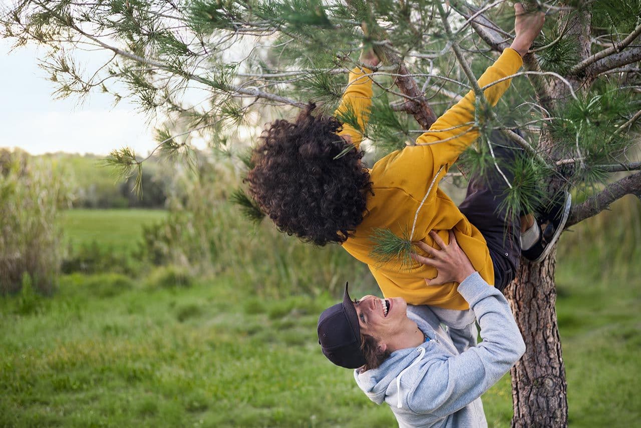 a man is helping a young boy climb a tree .