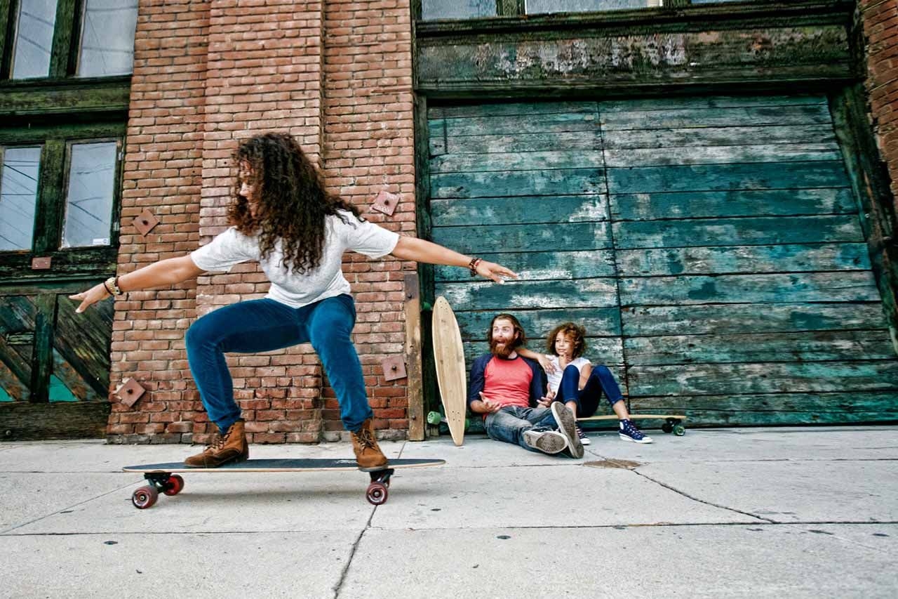 a man is riding a skateboard on a sidewalk while two men sit on skateboards .
