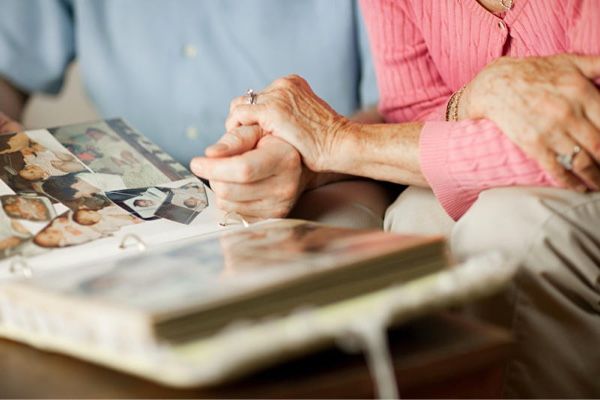 Older couple holding hands and looking at a photo album.