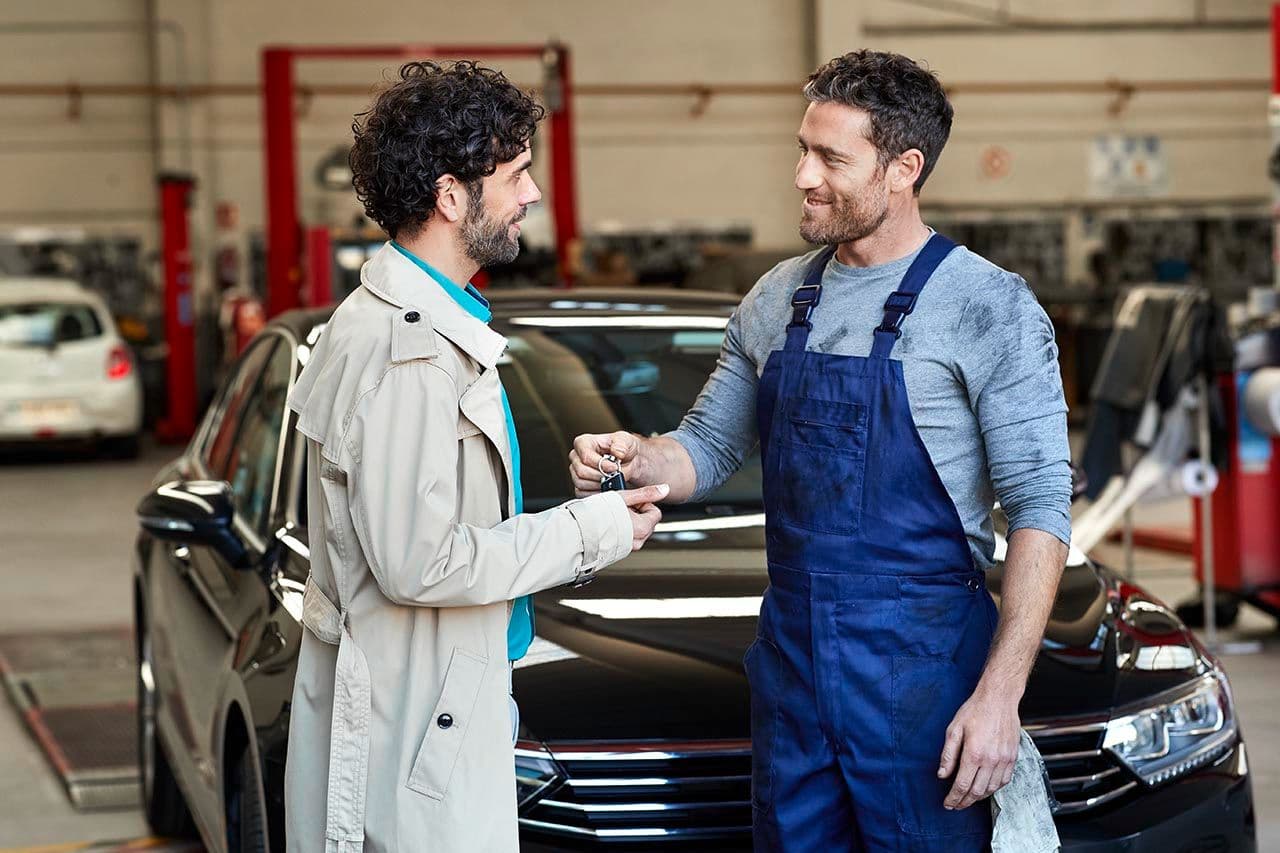 a man is giving a car key to a mechanic in a garage .