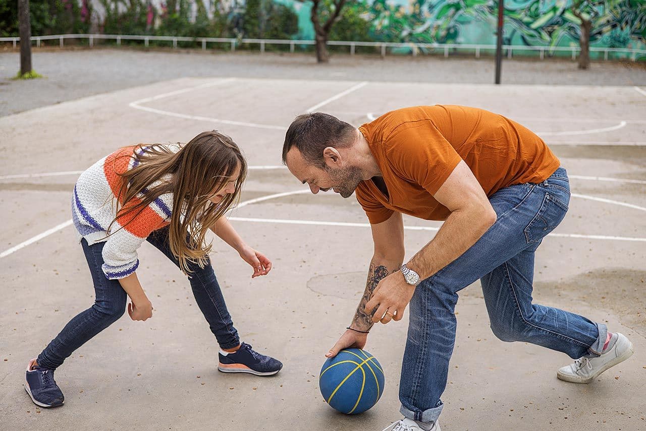 a man and a little girl are playing with a basketball on a court .
