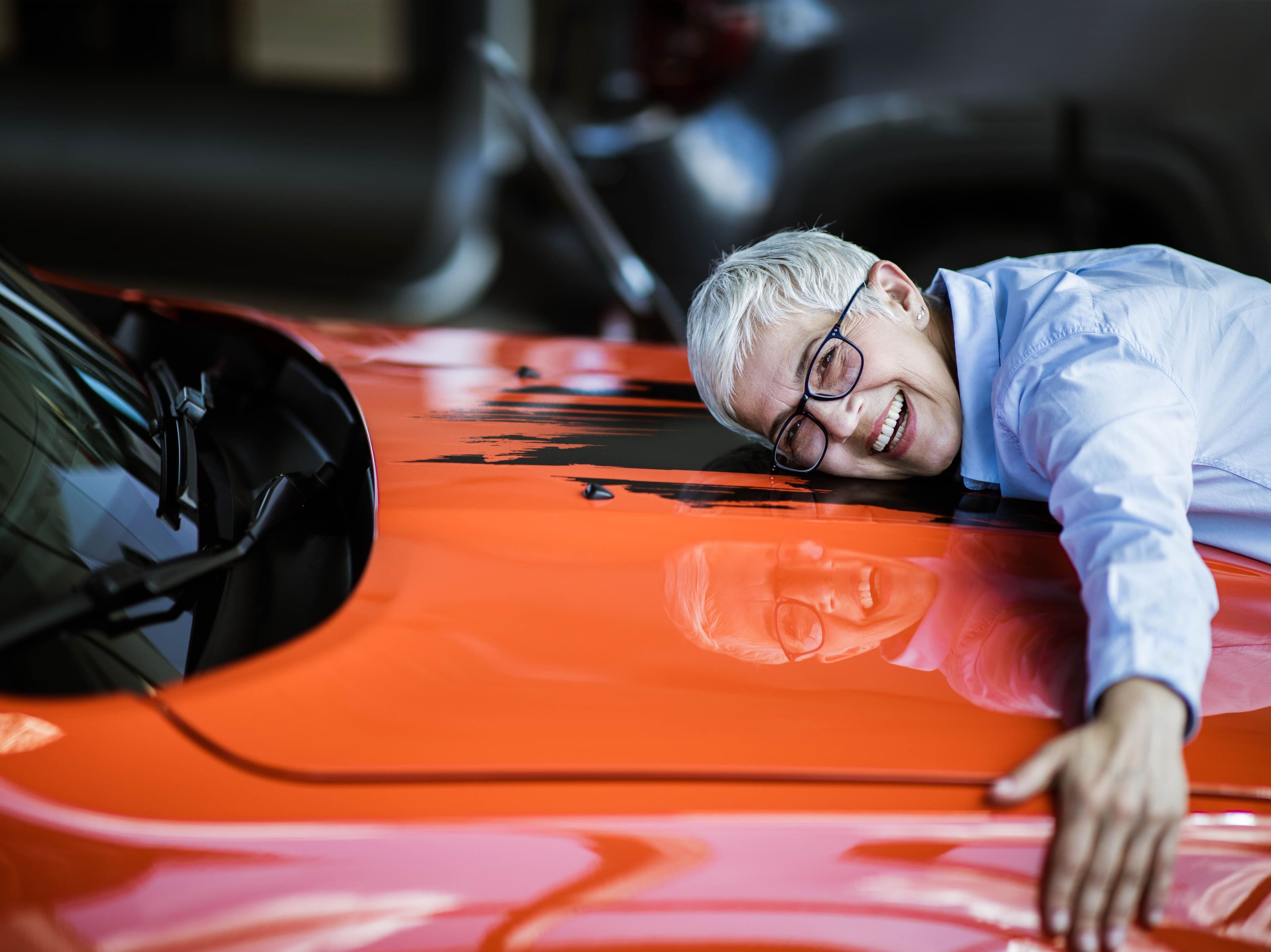 a man with glasses is leaning on the hood of a red car .