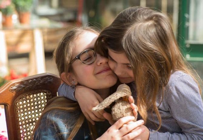 two young girls are hugging each other while holding a teddy bear .