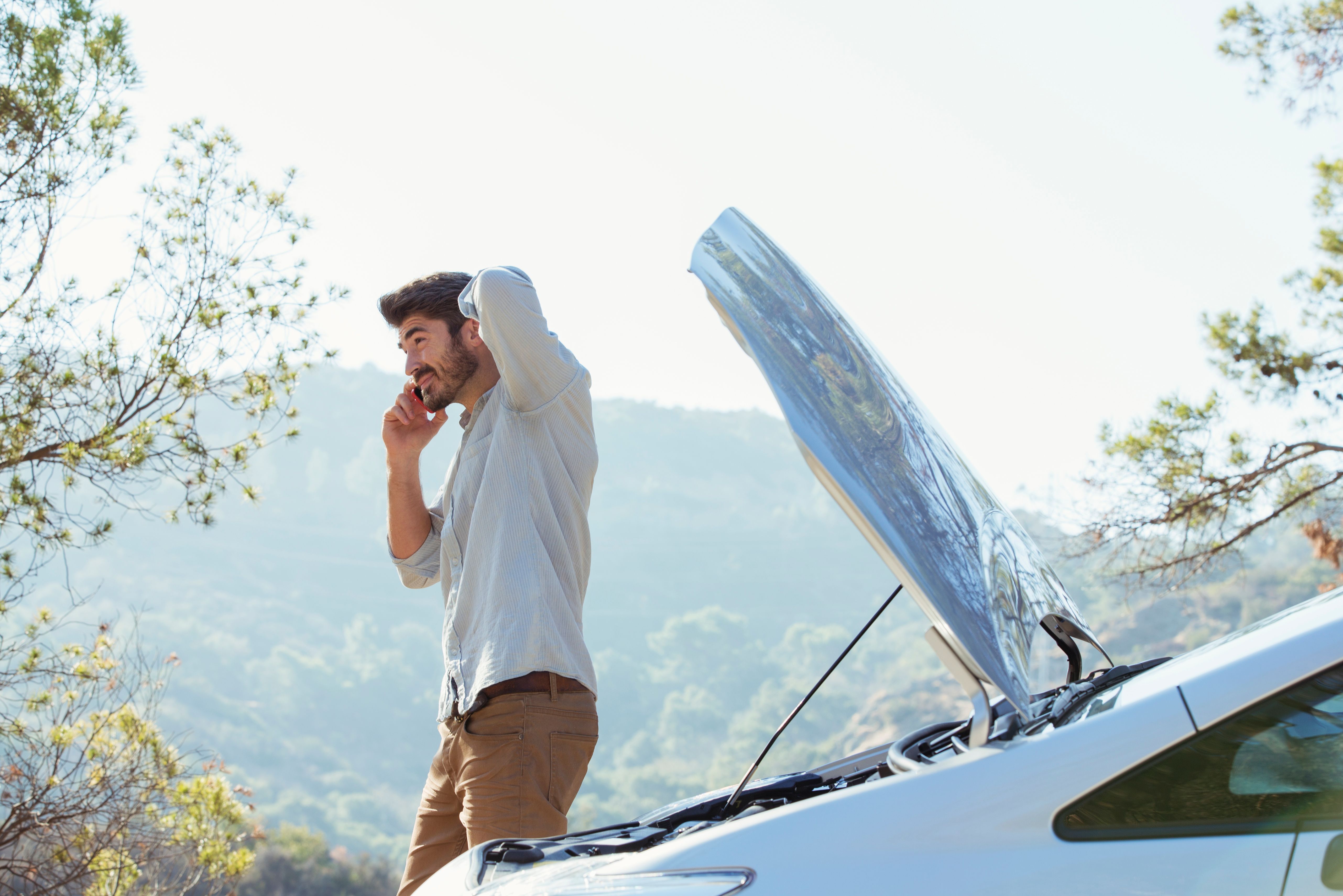 a man is standing next to a broken down car with the hood up and talking on a cell phone .