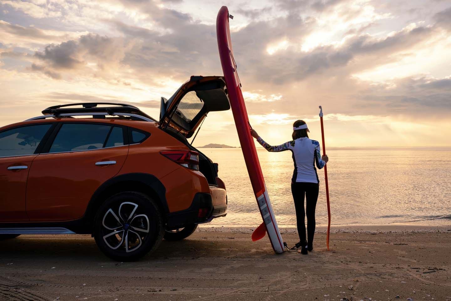 a woman is holding a surfboard next to a car on the beach .