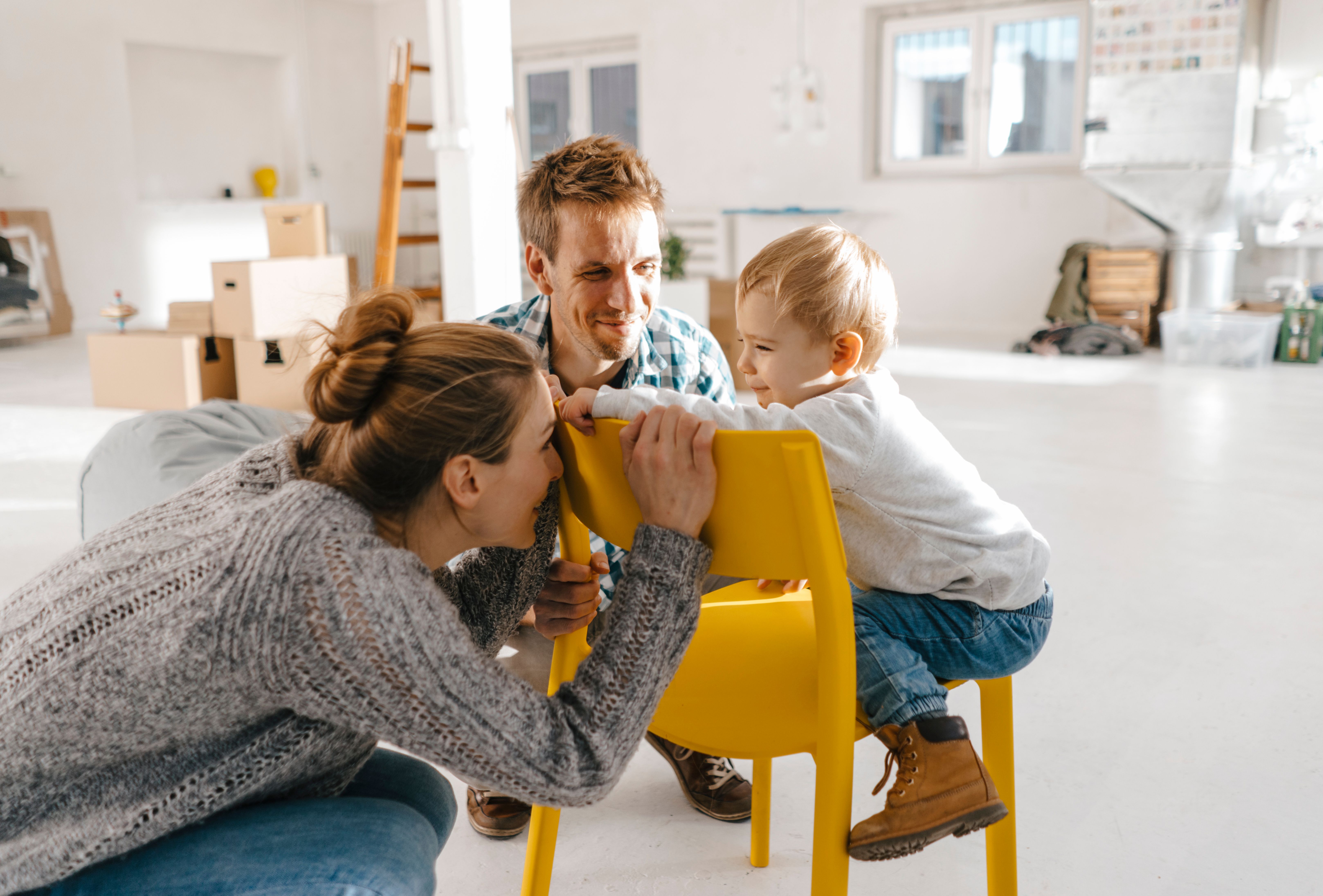 a family is playing with a yellow chair in their new home .